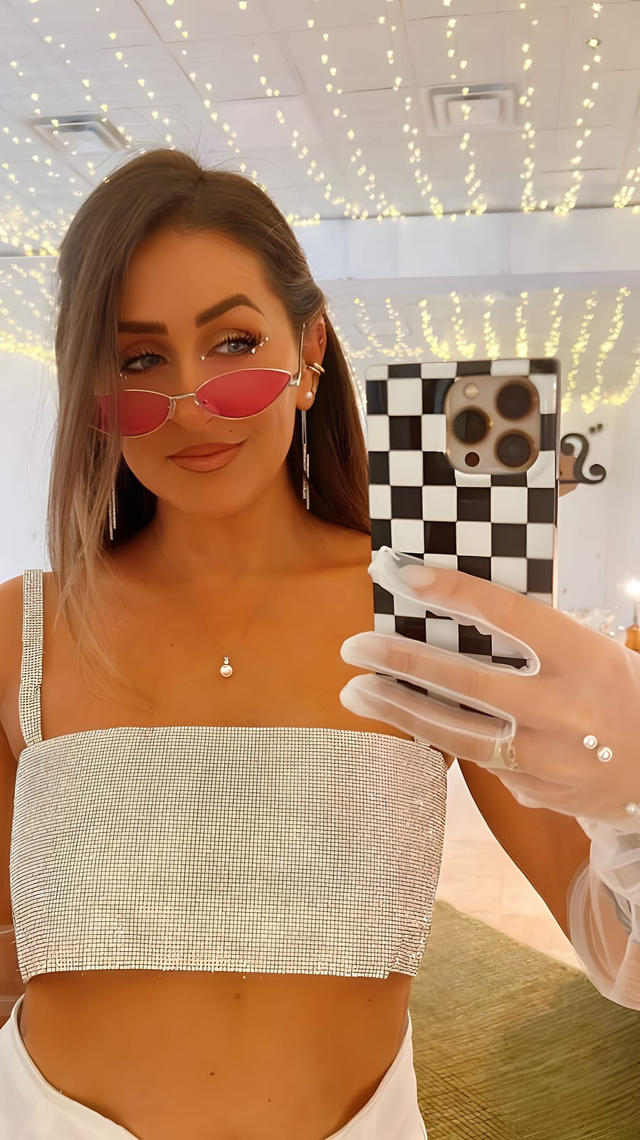 Mirror selfie of Cate in sunglasses and a sparkly top, string lights behind