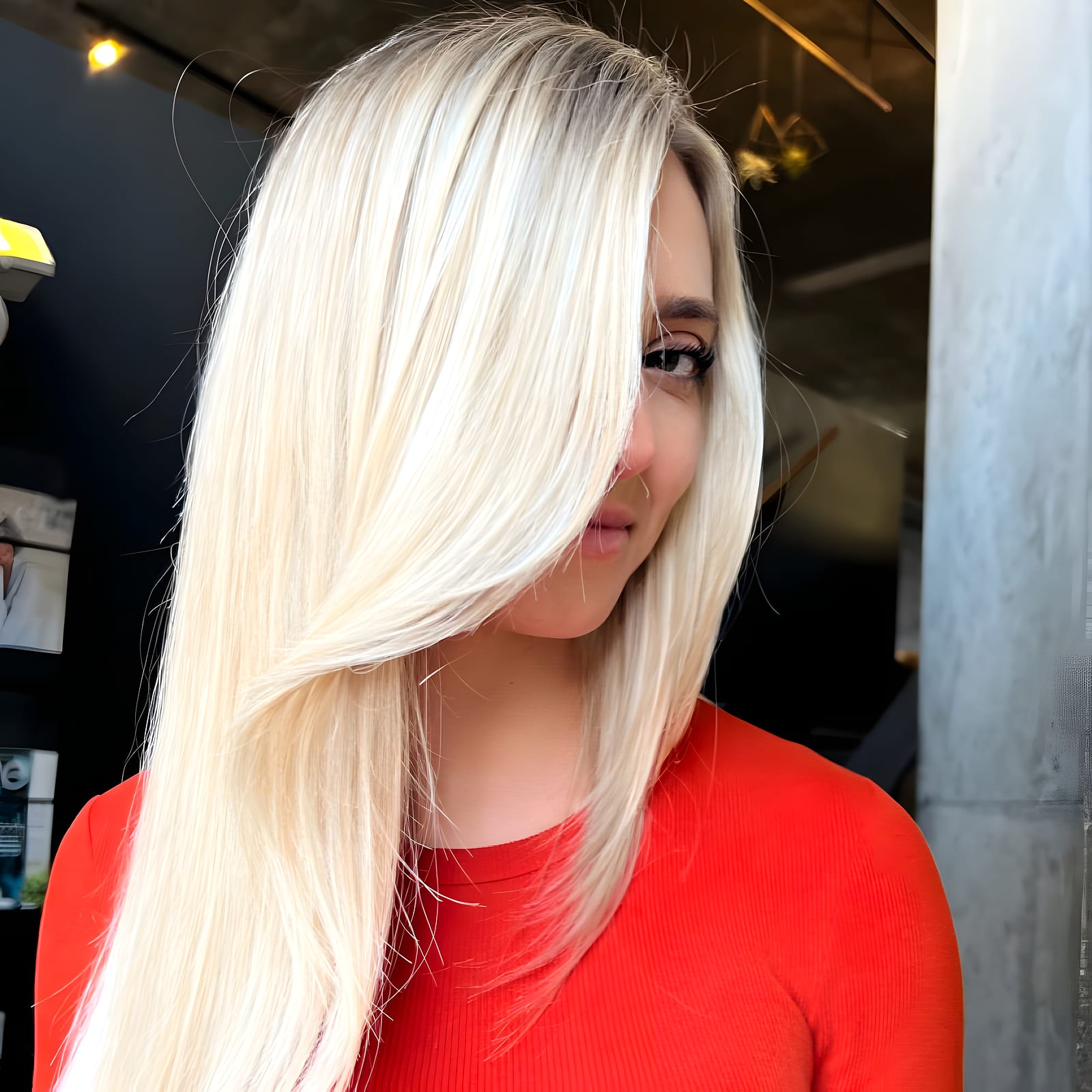 Woman with sleek platinum blonde hair partly covering her face, wearing a red top