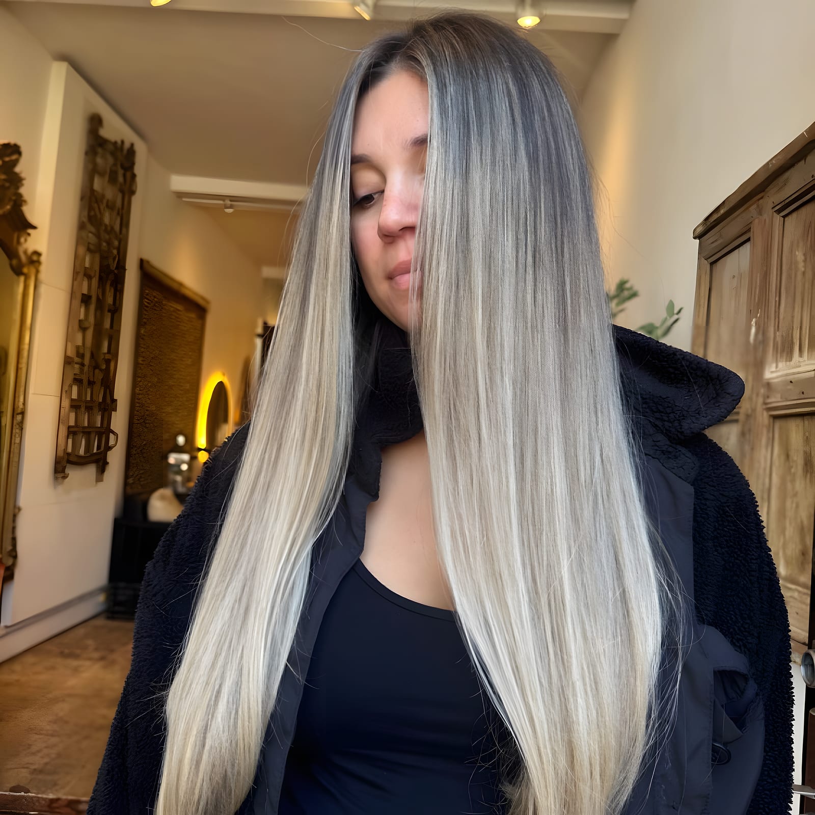 Woman with long straight blonde and grey balayage hair looking down in the salon hallway